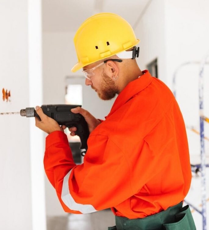 young foreman orange work clothes yellow hardhat using electric drill work new apartments